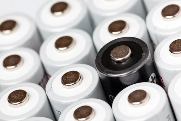 AA batteries are located close to each other. Close-up of all white batteries, except one black, on a white background. Battery technology.