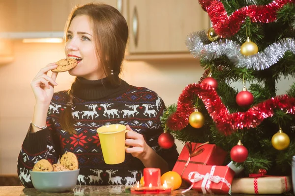 Junge glückliche Frau isst Schokokekse in der Nähe des Weihnachtsbaums — Stockfoto