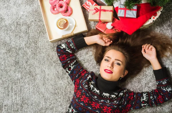 Junges nettes glückliches Mädchen im Pullover mit Hirschen, die zu Hause auf dem Boden liegen. Neujahrs- und Weihnachtsfeier — Stockfoto