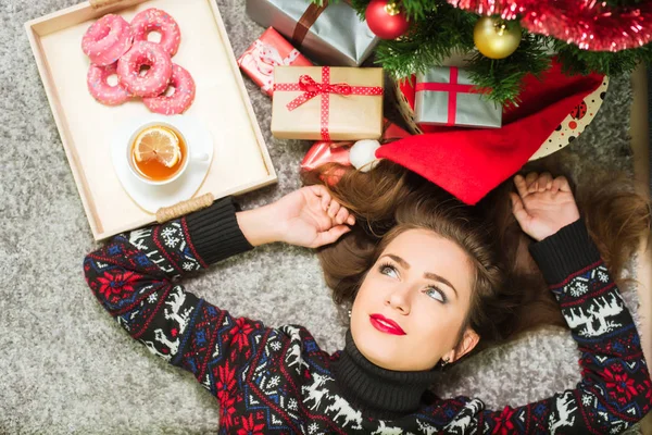 Junges nettes glückliches Mädchen im Pullover mit Hirschen, die zu Hause auf dem Boden liegen. Neujahrs- und Weihnachtsfeier — Stockfoto