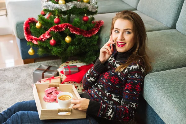 Joven hermosa mujer con un teléfono en el fondo del árbol de Navidad — Foto de Stock
