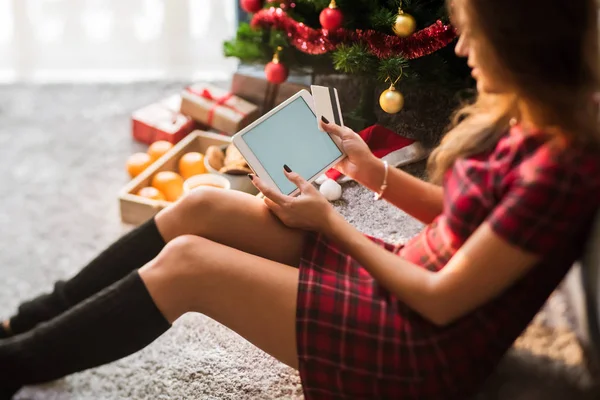 Woman holding tablet with blank space and credit card lying on floor. Christmas shopping concept