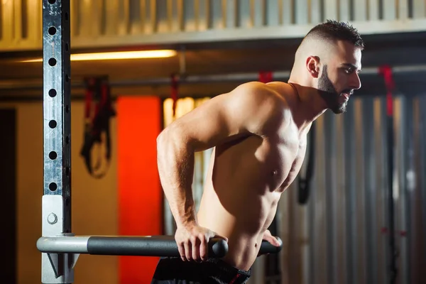 Homem musculoso trabalhando no ginásio fazendo exercícios em barras paralelas — Fotografia de Stock