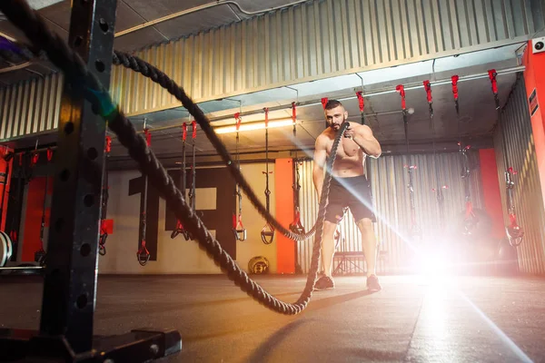 Joven hombre en forma haciendo ejercicio con cuerdas de batalla en el gimnasio de fitness —  Fotos de Stock