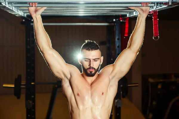 Atleta muscular ajuste homem puxando para cima no horizontal bar no um ginásio — Fotografia de Stock