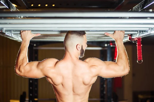 Atleta muscular ajuste homem puxando para cima no horizontal bar no um ginásio — Fotografia de Stock