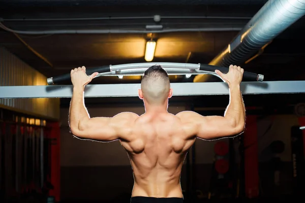 Atleta muscular ajuste homem puxando para cima no horizontal bar no um ginásio — Fotografia de Stock