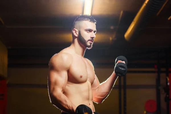 Muscular sem camisa jovem segurando halteres no ginásio — Fotografia de Stock