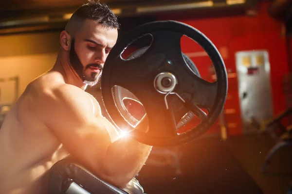 Mladý svalnatý muž trénink s činky a při pohledu na biceps — Stock fotografie