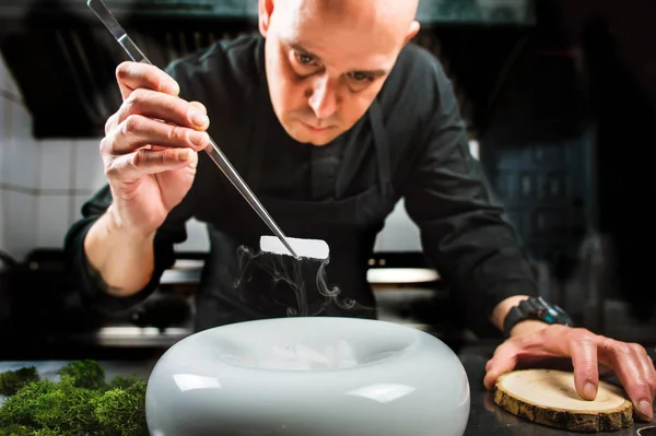 Chef se concentra en la preparación de plato molecular moderno con pinzas y nitrógeno líquido Imagen De Stock