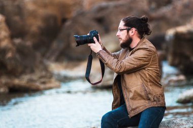 Kayanın üzerinde oturan ve deniz fotoğraf yapma uzun saç ve sakal ile genç şık fotoğraf.