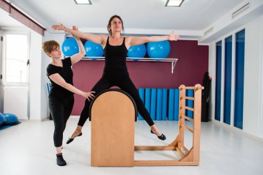 Kişisel eğitmen denetleyici genç kadın spor salonunda arka planda diğer pilates aletleri pilates merdiven varil üzerinde uzanan yerleştirmek. Fitness ve sağlıklı yaşam konsepti