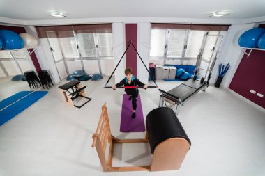 Boş ve geniş spor salonunda pilates egzersizleri yoga yaparken genç çekici kadın. Pilates ekipmanları arka plan üzerinde. Sağlıklı ve aktif yaşam tarzı kavramı
