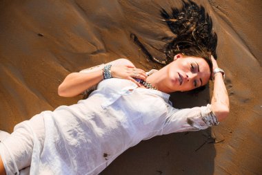 Üstten Görünüm seksi ve güzel esmer beyaz gömlek ve parlak takı ve yalan ve ıslak kum plaj poz. Deniz dalgaları. Moda beğenilen.