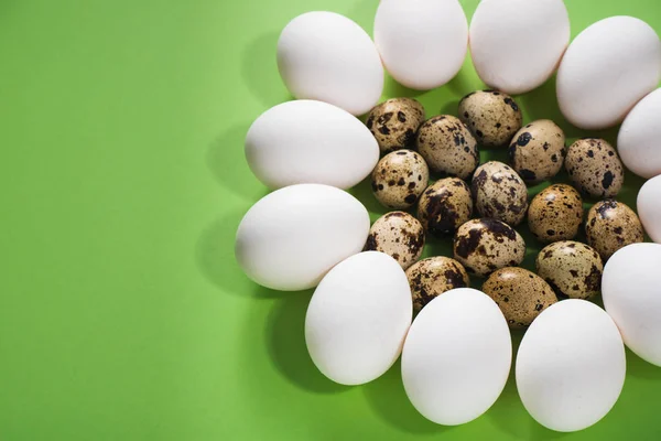 White chicken eggs laid out in a flower on green background