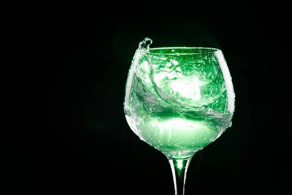 Spruzzare acqua nel bicchiere di vino con sfondo verde — Foto Stock