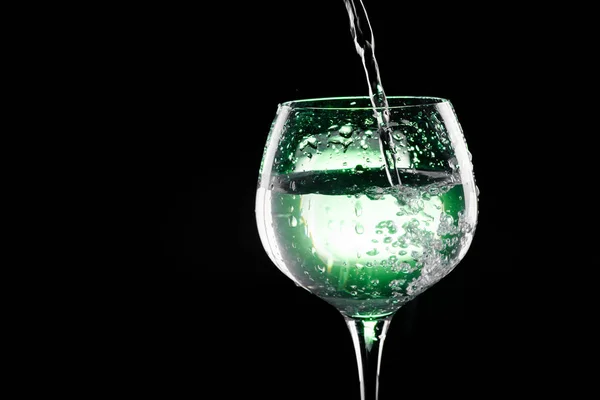 Despejar água no copo de vinho com fundo verde — Fotografia de Stock