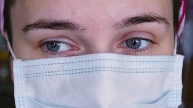 Tıbbi koruyucu maskeli, kameraya bakan üzgün genç bir kadının yakın çekimi. Koronavirüs salgını sırasında yorgun doktor. Covid-19 karantina konsepti.