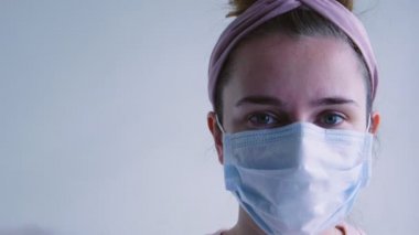 Tıbbi maskeli genç bir kadın kameraya bakıyor, maskeyi çıkarıyor ve gülümsüyor. Covid-19 konsepti. Koronavirüs salgınının sonu ve karantina.