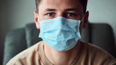 Tıbbi maske takan ve kameraya bakan genç adamın yakın plan portresi. Coronavirus, Covid-19, 2019-NCoV salgını. Karantina.