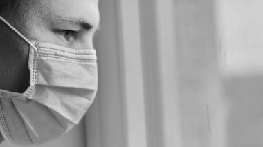 Tek renkli, tıbbi maskeli genç bir doktorun umutsuzluk içinde pencereden dışarı bakışı. Coronavirus, Covid-19, 2019-NCoV salgını. Karantina, evde kal. Boşluğu kopyala.