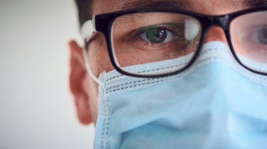 Genç üzgün ve yorgun doktorun sisli gözlüklü ve tıbbi maske takmış kameraya bakarken yakın plan portresi. Coronavirus, Covid-19, 2019-NCoV salgını. Karantina, evde kal. Boşluğu kopyala.
