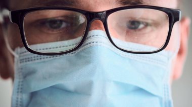 Genç üzgün ve yorgun doktorun sisli gözlüklü ve tıbbi maske takmış kameraya bakarken yakın plan portresi. Coronavirus, Covid-19, 2019-NCoV salgını. Karantina, evde kal. Boşluğu kopyala.
