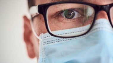 Tıbbi maskeli ve gözlüklü genç adam kameraya bakıyor. Tıbbi sistem çöktü. Coronavirus, 2019-ncov, covid-2019 salgını. Karantina.