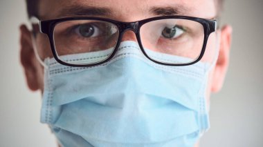 Genç üzgün ve yorgun doktorun sisli gözlüklü ve tıbbi maske takmış kameraya bakarken yakın plan portresi. Coronavirus, Covid-19, 2019-NCoV salgını. Karantina, evde kal. Boşluğu kopyala.