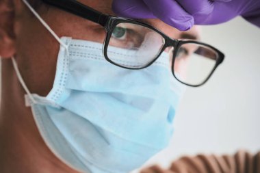 Tıbbi maskeli genç bir doktor, sisli bardaklar ve bertaraf eldivenleri. Coronavirus, Covid-19, 2019-NCoV salgını. Tıbbi sistem çöktü. Karantina, evde kal. Boşluğu kopyala.