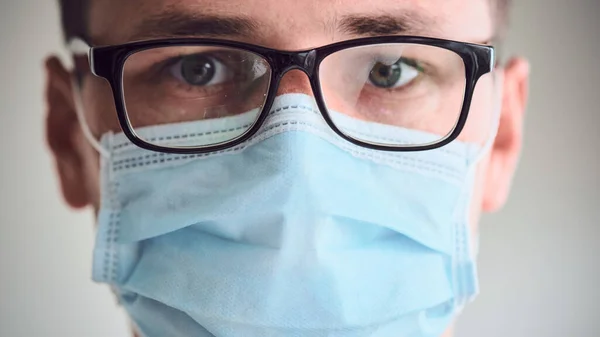 Genç üzgün ve yorgun doktorun sisli gözlüklü ve tıbbi maske takmış kameraya bakarken yakın plan portresi. Coronavirus, Covid-19, 2019-NCoV salgını. Karantina, evde kal. Boşluğu kopyala.
