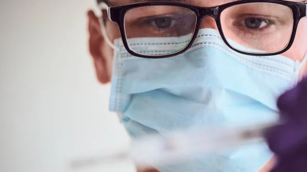 Gözlüklü, tıbbi maskeli ve tek kullanımlık eldivenli genç adam beyaz arka planda izole edilmiş termometreye bakıyor. Coronavirus, Covid-19, 2019-NCoV salgını. Karantina, evde kal. Boşluğu kopyala.
