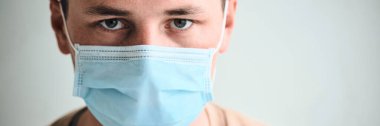 Tıbbi maskeli genç adamın portresi beyaz arka planda izole edilmiş kameraya bakıyor. Coronavirus, Covid-19, 2019-NCoV salgını. Karantina, evde kal. Boşluğu kopyala.