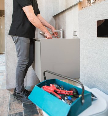 Aletleri olan tesisatçı ön plandaki musluk suyu alet kutusunu tamir ediyor.