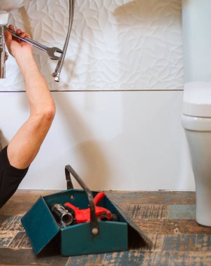Tesisatçı banyodaki lavabo borusunu tamir ediyor, çekmecede yerde profesyonel aletler var.