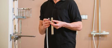 Koyu renk tişörtlü bir adam duş odası için su karıştırıcısını tutuyor.