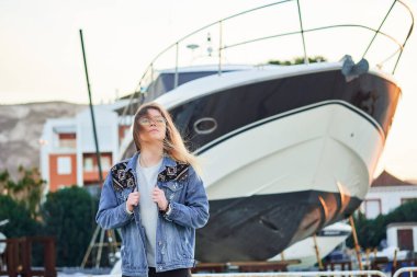 Güneş gözlüklü güzel bir kız ve uzun sarı saçlı yaz günbatımında büyük lüks bir yatın arka planında.