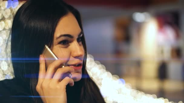 Chica morena joven hablando por teléfono en el centro comercial en el fondo de luces brillantes — Vídeos de Stock