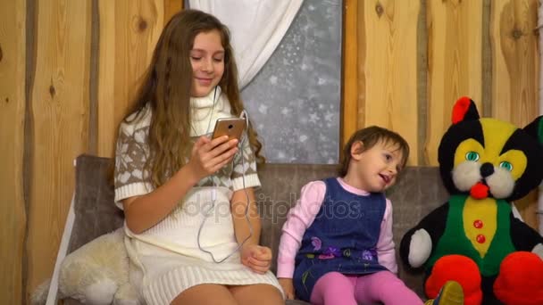 Dospívající dívka s malou sestřičku poslech hudby ze smartphonu doma — Stock video