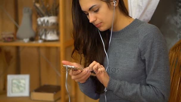 Chica joven con auriculares escuchando música desde un teléfono inteligente y canta en casa — Vídeos de Stock