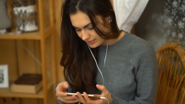 Mladá dívka se sluchátky na poslech hudby ze smartphonu a zpívá doma — Stock video