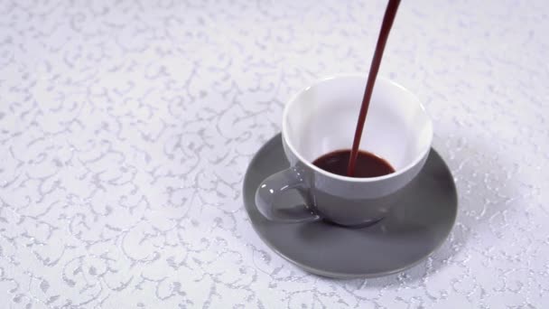 Cup står på en vit mönstrad duk och kaffe hälls i det — Stockvideo