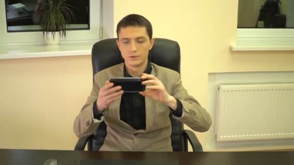 Joven empleado toma un teléfono sentado en una silla en una mesa — Vídeos de Stock
