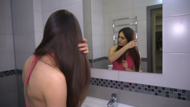 Menina está de pé no espelho e penteia o cabelo — Vídeo de Stock