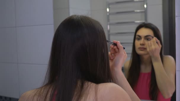 Chica morena haciendo maquillaje de cejas mirando en el espejo del baño — Vídeos de Stock