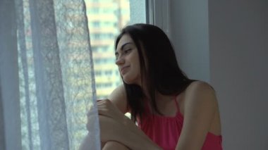 Genç kadın gülümseyen ve üzgün pencereden dışarı bakarak