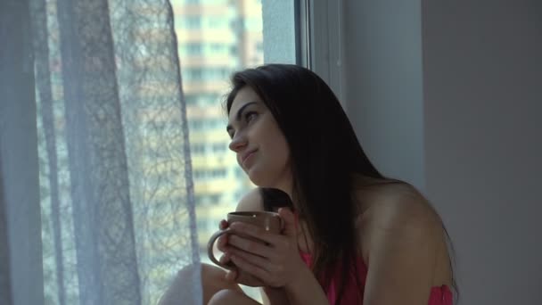 Chica es soñadoramente triste mirando por la ventana y beber café — Vídeo de stock