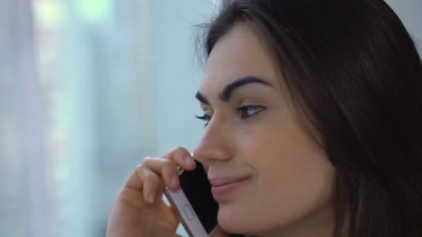 Hermosa morena hablando por teléfono sentada junto a la ventana de cerca — Vídeos de Stock