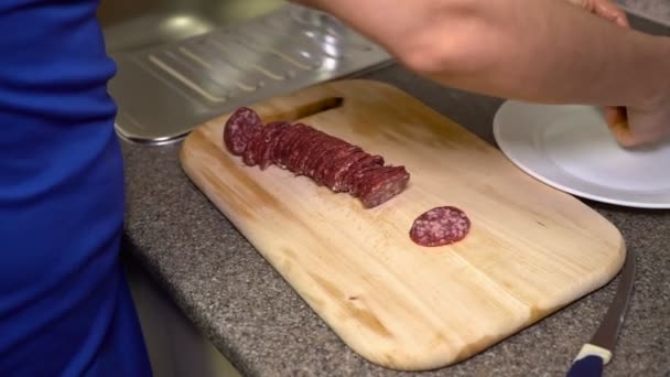 Mädchen schneidet Salami und legt auf einen Teller — Stockvideo