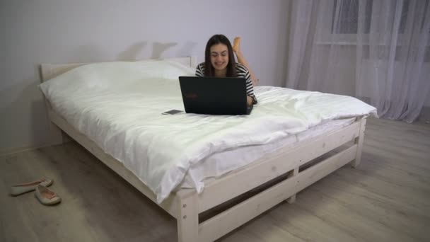 Щаслива дівчина спілкується на ліжку лежить і рухає ноги — стокове відео